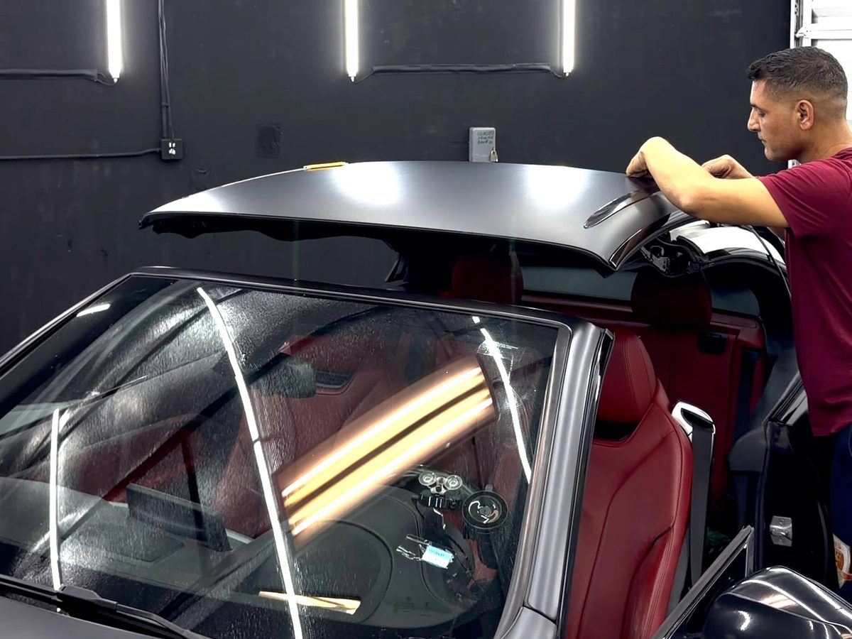 Elite Wrap installer at work on a satin grey convertible in the bay