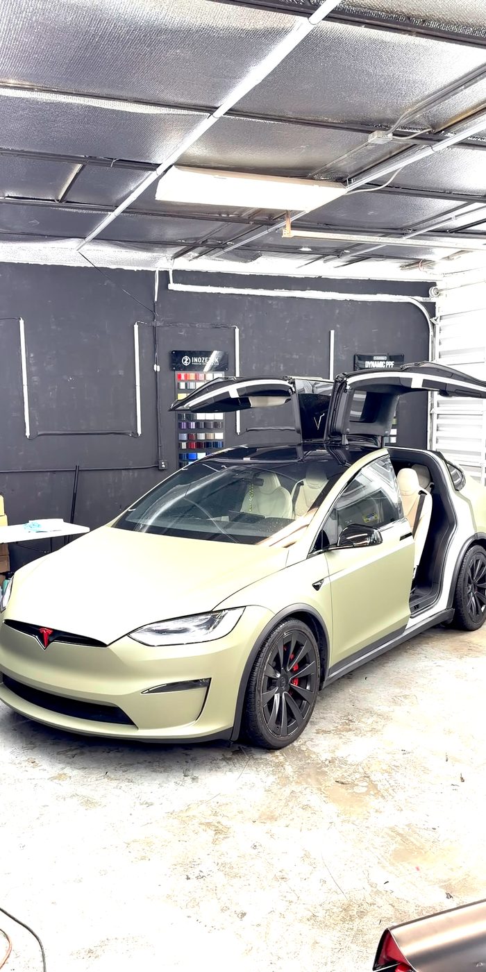 Tesla Model X in a sage green wrap with the falcon doors up