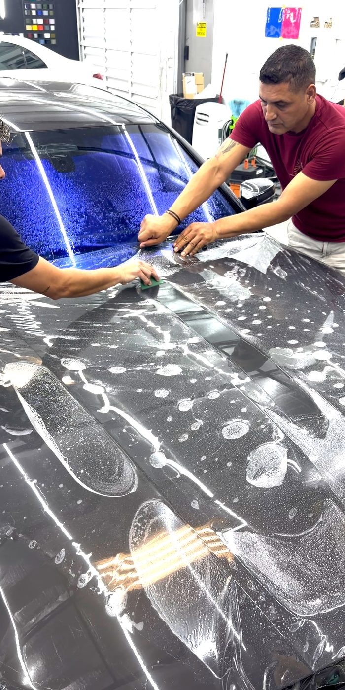 Two installers laying paint protection film on a hood