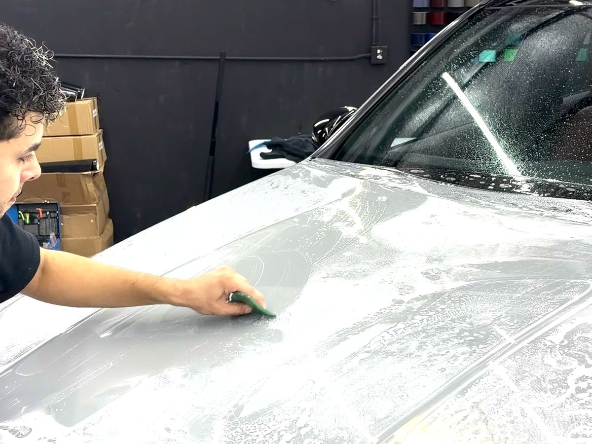 Installer squeegeeing paint protection film onto a hood at Elite Wrap