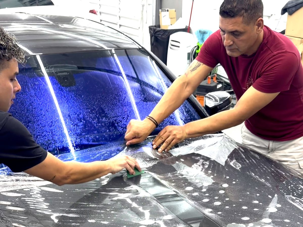 Two installers laying paint protection film on a hood