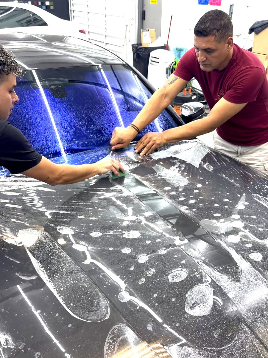 Two installers laying paint protection film on a hood